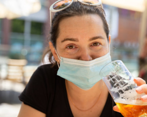 Woman in protective mask enjoying beer at outdoor bar terrace